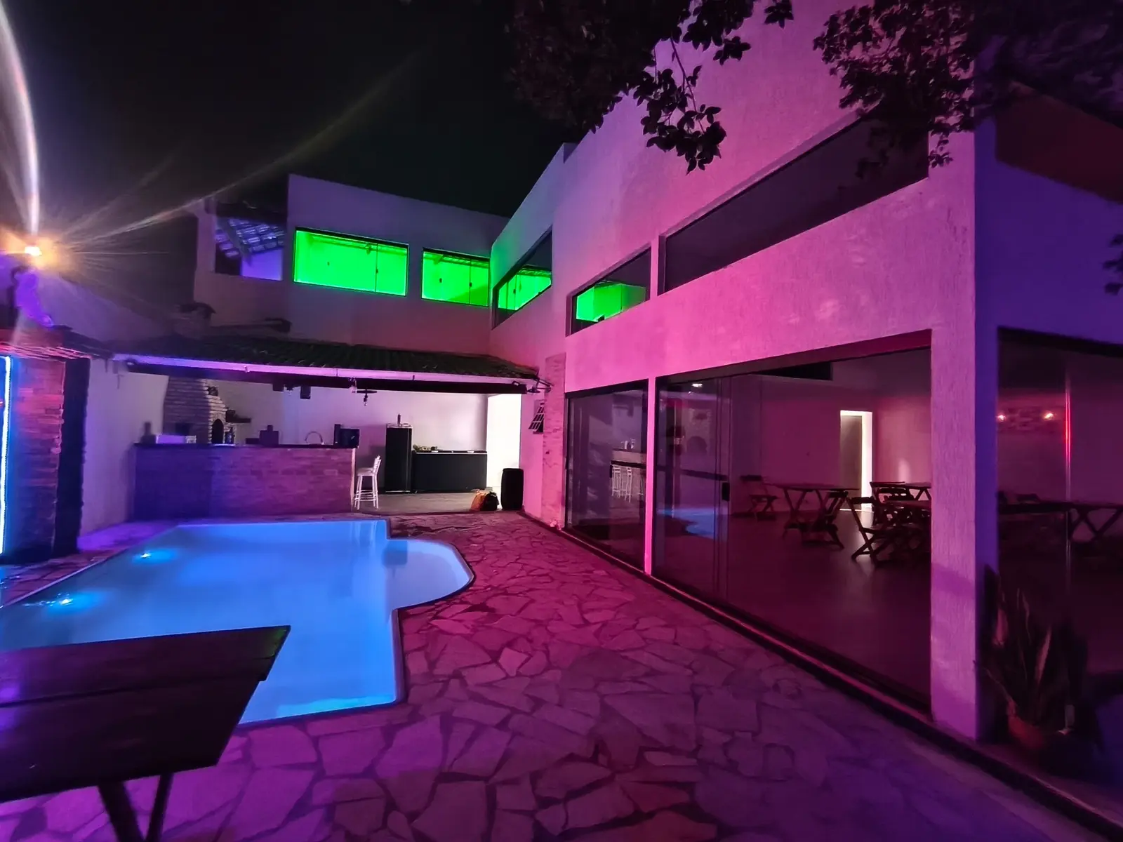 Piscina e salão da Casa Góes iluminados à noite